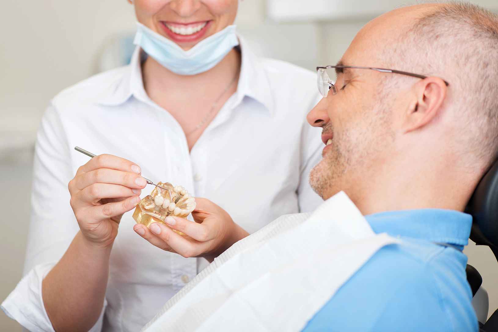 Smiling female dentist explaining artificial teeth to patient in clinic