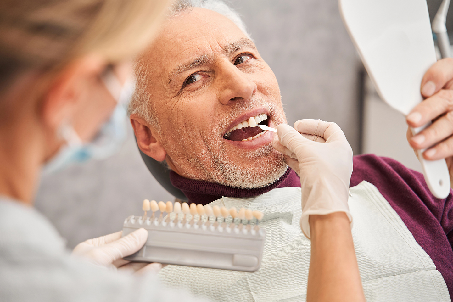 The dentist talking with the patient about dental care and selects the patient the color of the tooth enamel at the stomatology cabinet. Stock photo